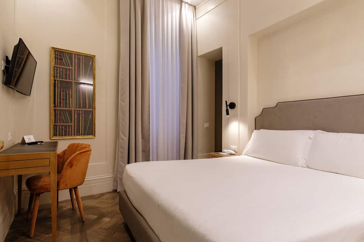 Une chambre d’hôtel équipée d’un lit, d’un bureau, d’une chaise, d’une télévision et d’une bibliothèque.
