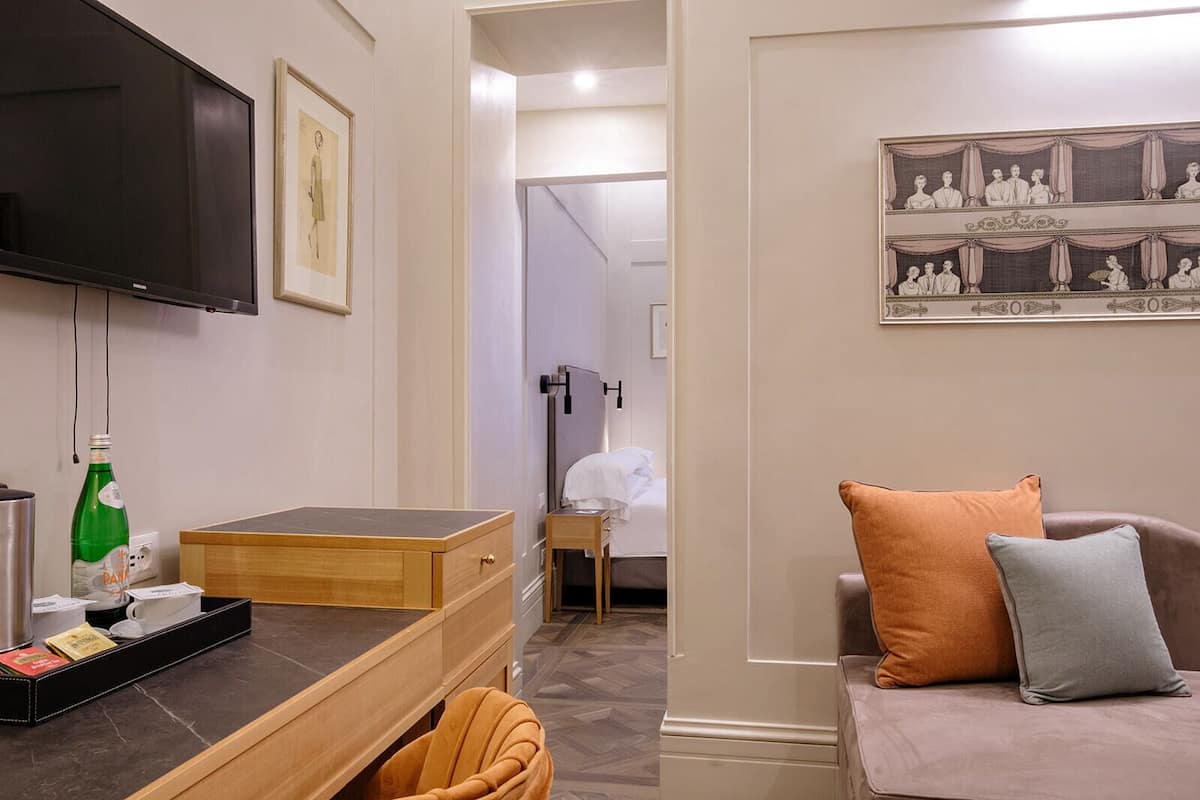 Une chambre d’hôtel avec un bureau en bois, un téléviseur à écran plat, un lit recouvert d’une couette blanche et un tableau au mur.