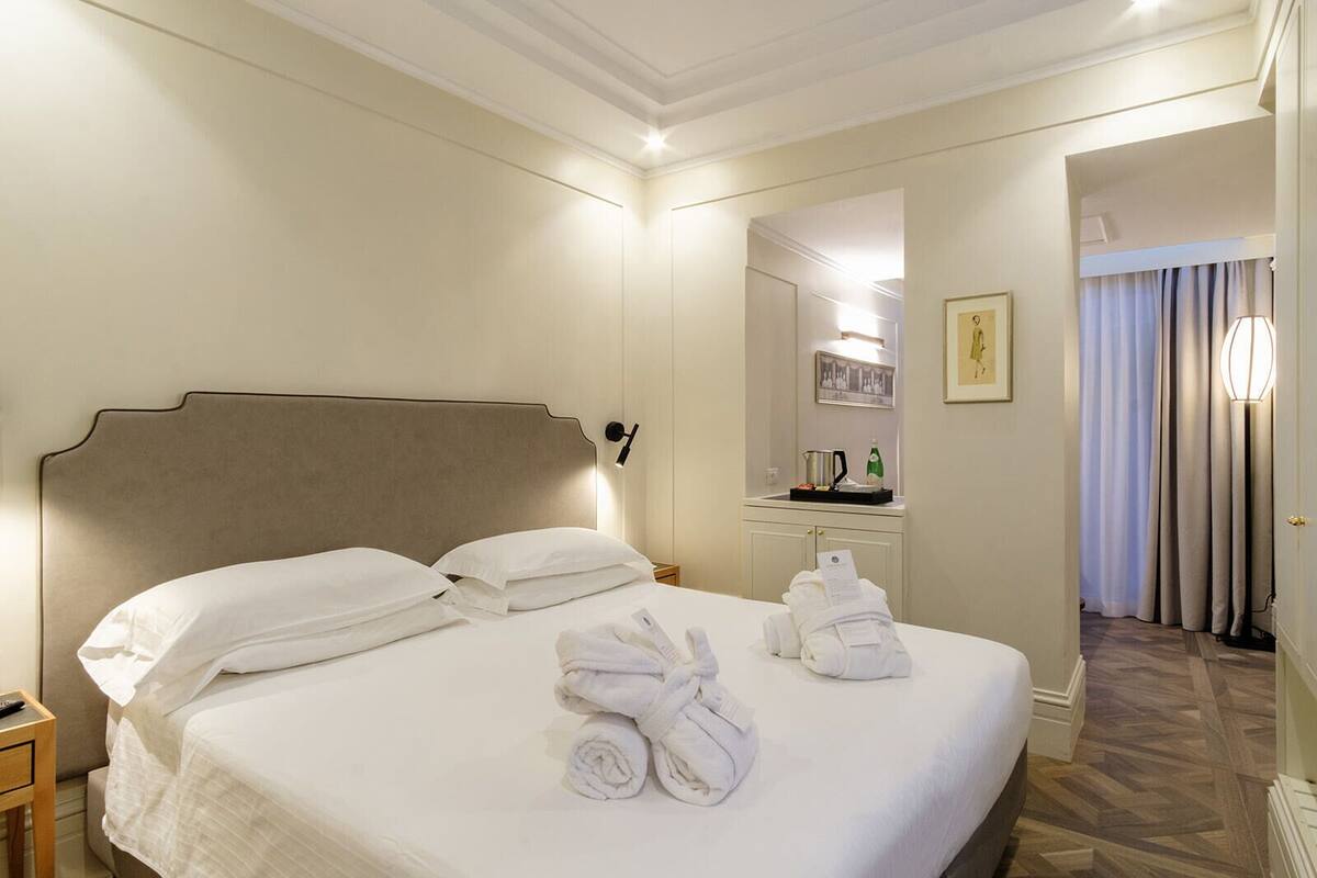 Une chambre d’hôtel avec un grand lit, une table de chevet, un miroir, une commode et une salle de bain visible à travers une porte ouverte.