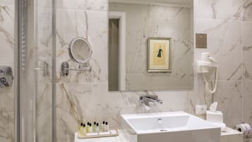 Un baño con ducha envuelta en vidrio, un lavabo blanco, un espejo y un cuadro enmarcado en la pared.