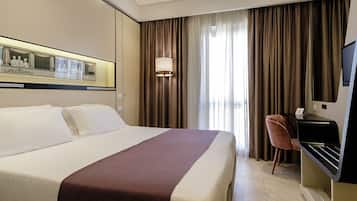 Habitación de hotel con una cama grande, un escritorio con silla, un televisor y una ventana con cortinas.