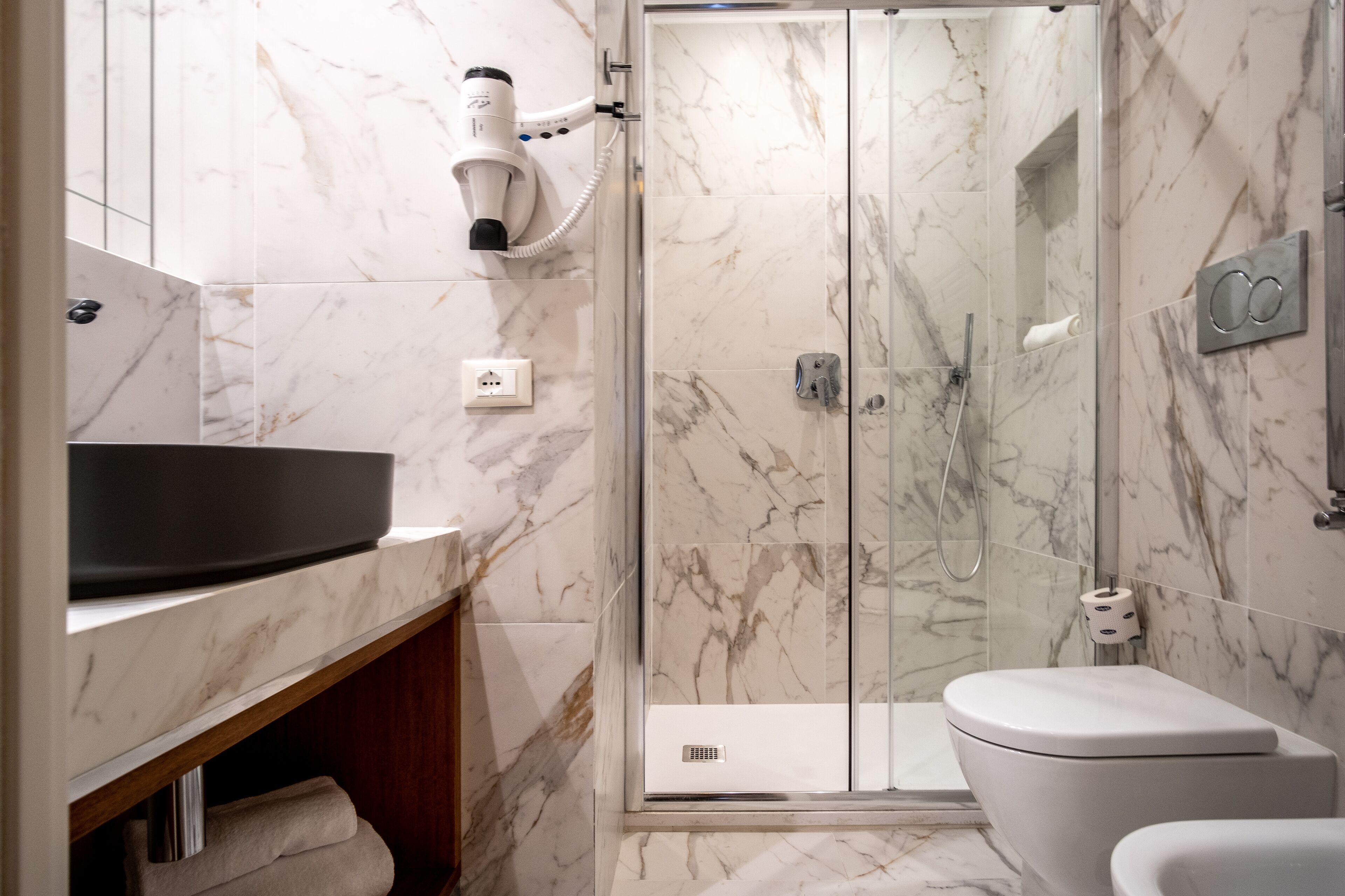 A modern bathroom with a marble shower enclosure, a standalone sink, and a toilet.