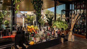 Zona de bar con varias botellas, un frutero y plantas colgantes.