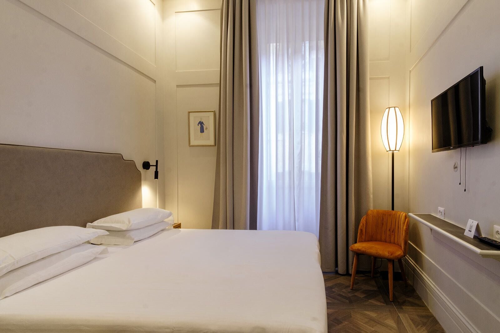 A hotel room with a large bed, a desk with a chair, a flat-screen TV, and a window with curtains.