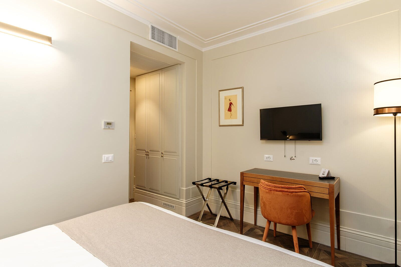A hotel room with a bed, a desk, a chair, a TV, and a lamp.