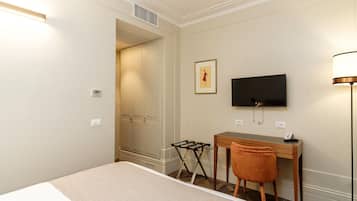 A hotel room with a bed, a desk, a chair, a TV, and a lamp.