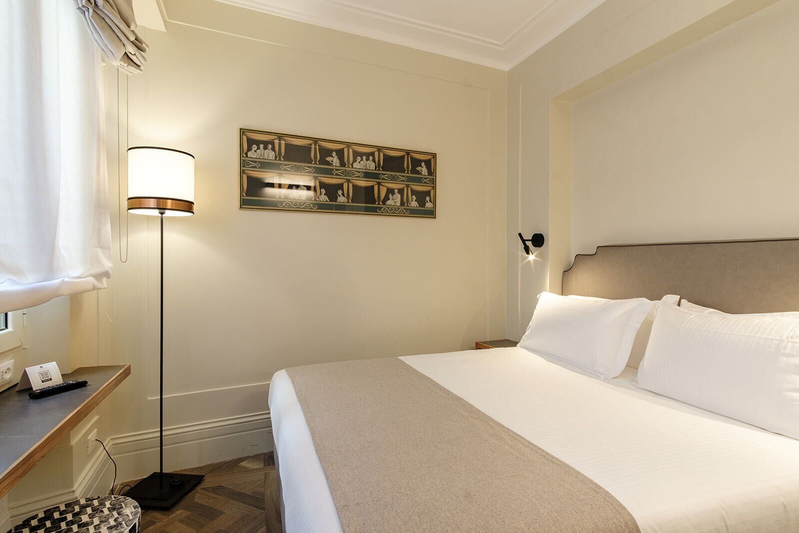Une chambre d’hôtel avec un lit, une table de chevet, une lampe, un tableau au mur et une fenêtre avec des rideaux.