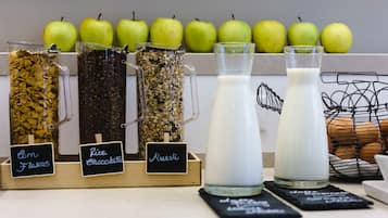 Une présentation de divers produits alimentaires, notamment des céréales de maïs, des barres de riz au chocolat et du muesli, avec un pichet de lait et des pommes en arrière-plan.
