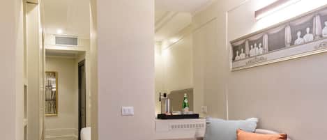 Un salon moderne avec un canapé, une petite table d’appoint et une étagère murale sur laquelle se trouvent une bouteille et une télécommande.
