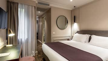 A hotel room with a bed, a desk with a lamp, a mirror, and a view of the hallway.