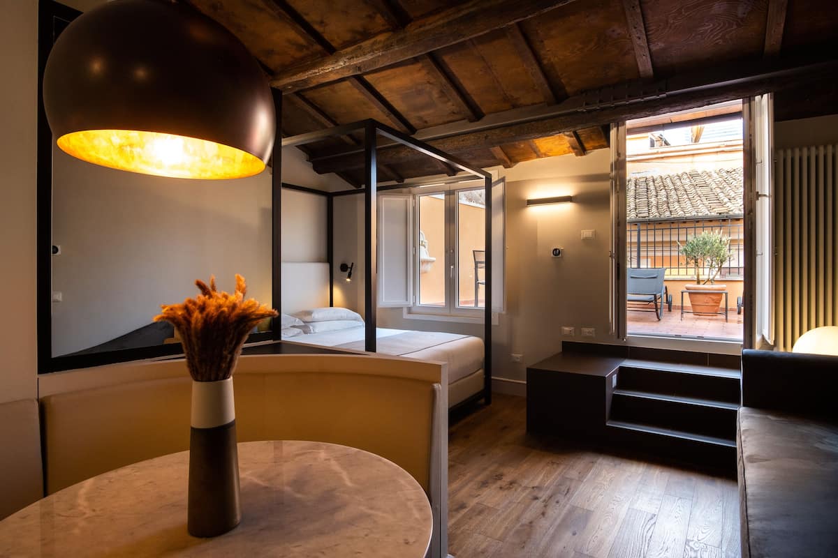 Un intérieur moderne avec une table ronde, un vase de fleurs séchées, un lit, un escalier et une vue sur l’extérieur.