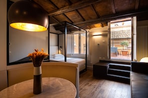 Un interior moderno con una mesa redonda, un florero con flores secas, una cama, una escalera y vistas al exterior.