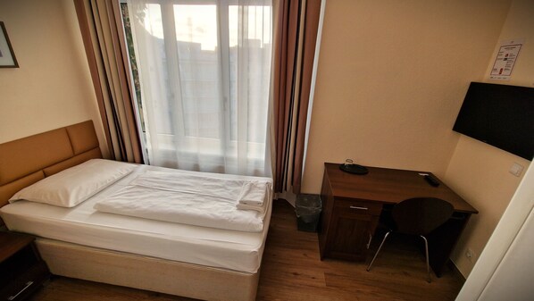 Habitación de hotel con cama, escritorio, silla, televisión y ventana con cortinas.
