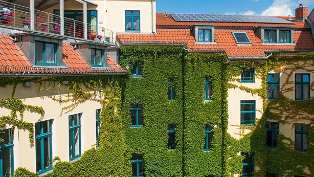 A building with multiple windows, some covered in ivy, and a balcony with chairs and flowers. - Mikon Eastgate Hotel (Berlin)