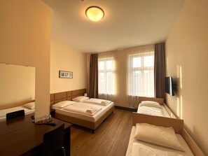 Habitación de hotel con dos camas, un escritorio, una silla, un televisor y una ventana con cortinas.