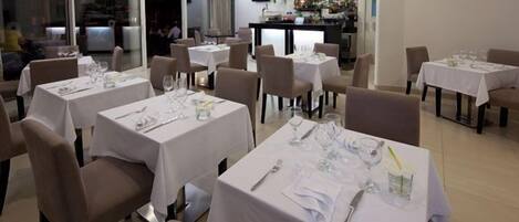 A restaurant with multiple tables set for dining, each with white tablecloths and basic tableware.