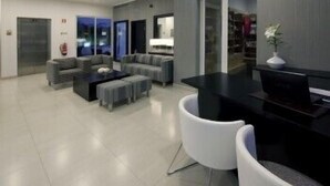 A modern hotel lobby with a seating area, a reception desk, and a large window. - Hotel White Waters (Machico)