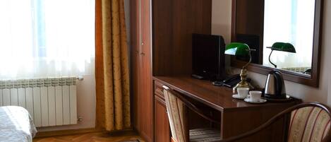 Une chambre d’hôtel avec un bureau en bois, une chaise, un lit, un radiateur, une fenêtre avec des rideaux et un miroir.