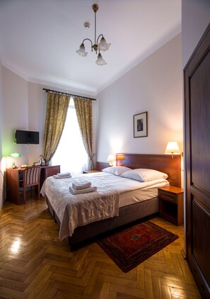 A hotel room with a bed, bedside lamps, a desk with a chair, a television, and a window with curtains.