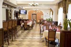 A restaurant with checkered flooring, wooden chairs, and tables set with red and white tablecloths.