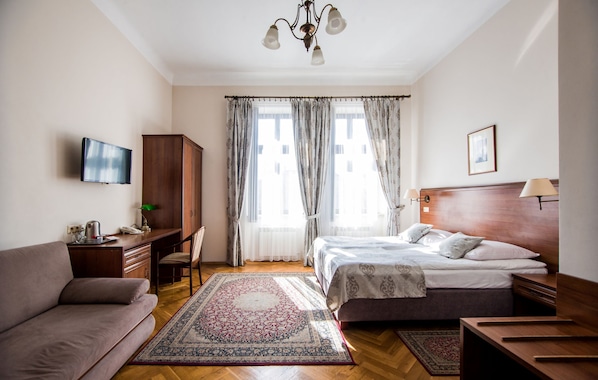 A bedroom with a bed, a desk, a chair, a television, and a large window with curtains.