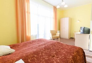 Habitación de hotel con cama, sillón, armario y escritorio con televisor.