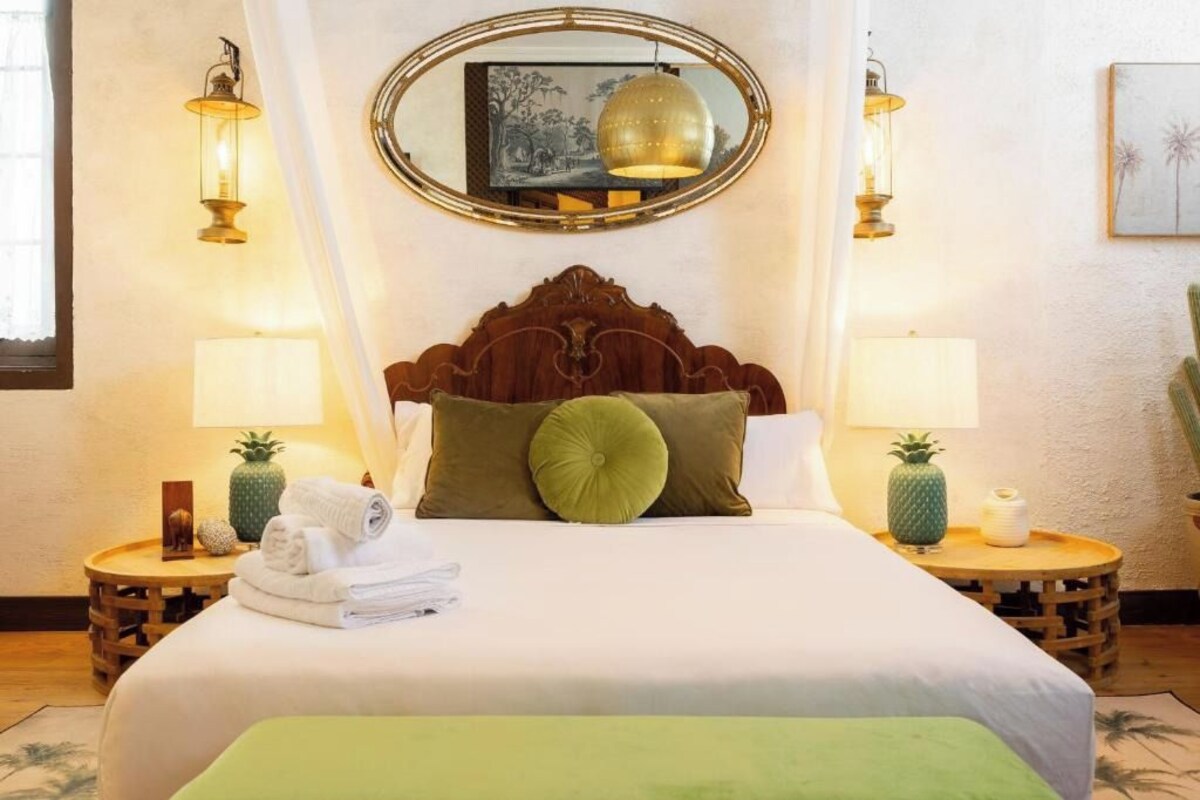 Una habitación de hotel con una cama grande, dos mesitas de noche, un espejo y lámparas de pared.