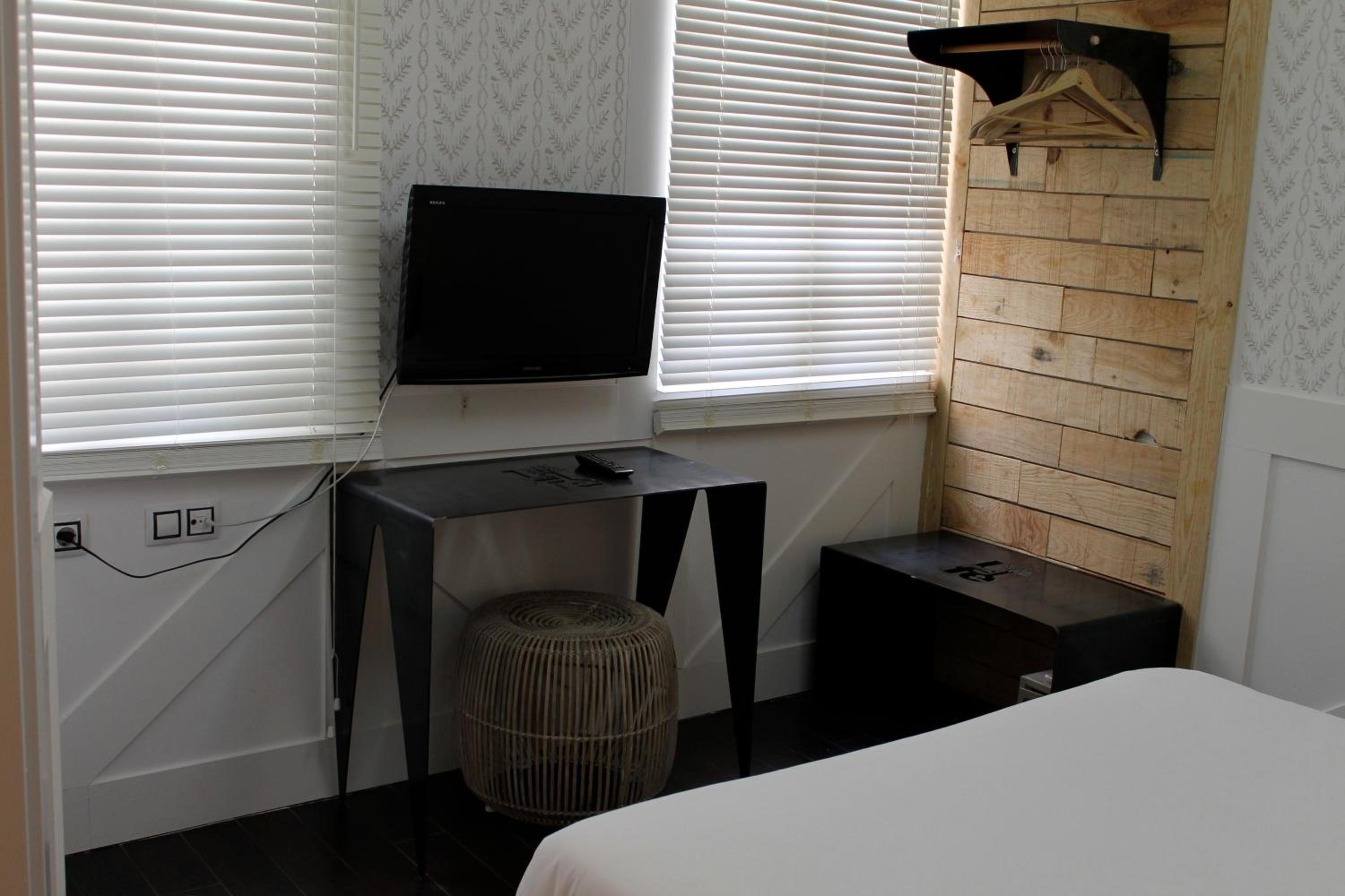 A bedroom with a bed, a TV mounted on the wall, a small table, and a hanging rack.