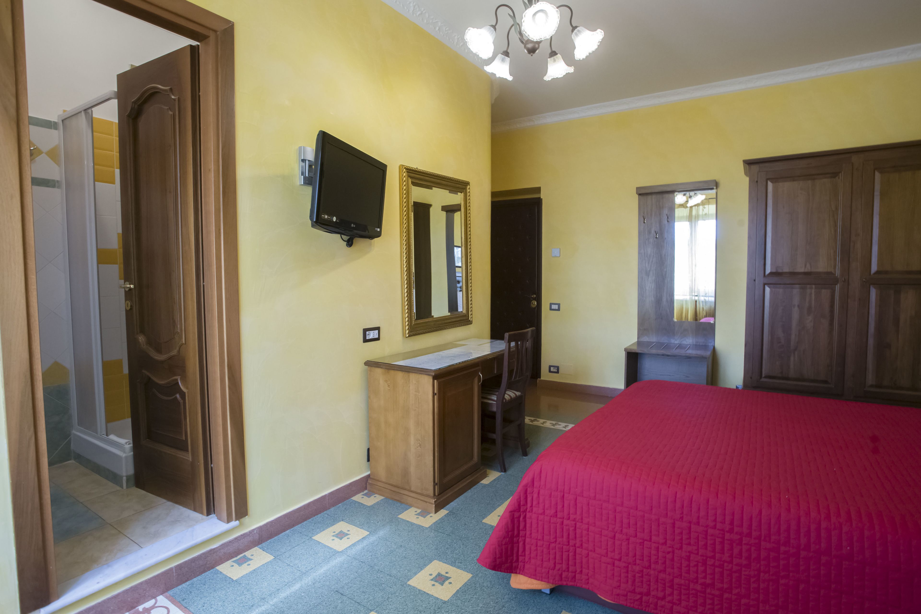 Una habitación de hotel con una cama, un escritorio de madera, una silla, un televisor y un espejo.