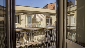 En balkon med gelændere og udsigt til en bygning med en stribet markise.