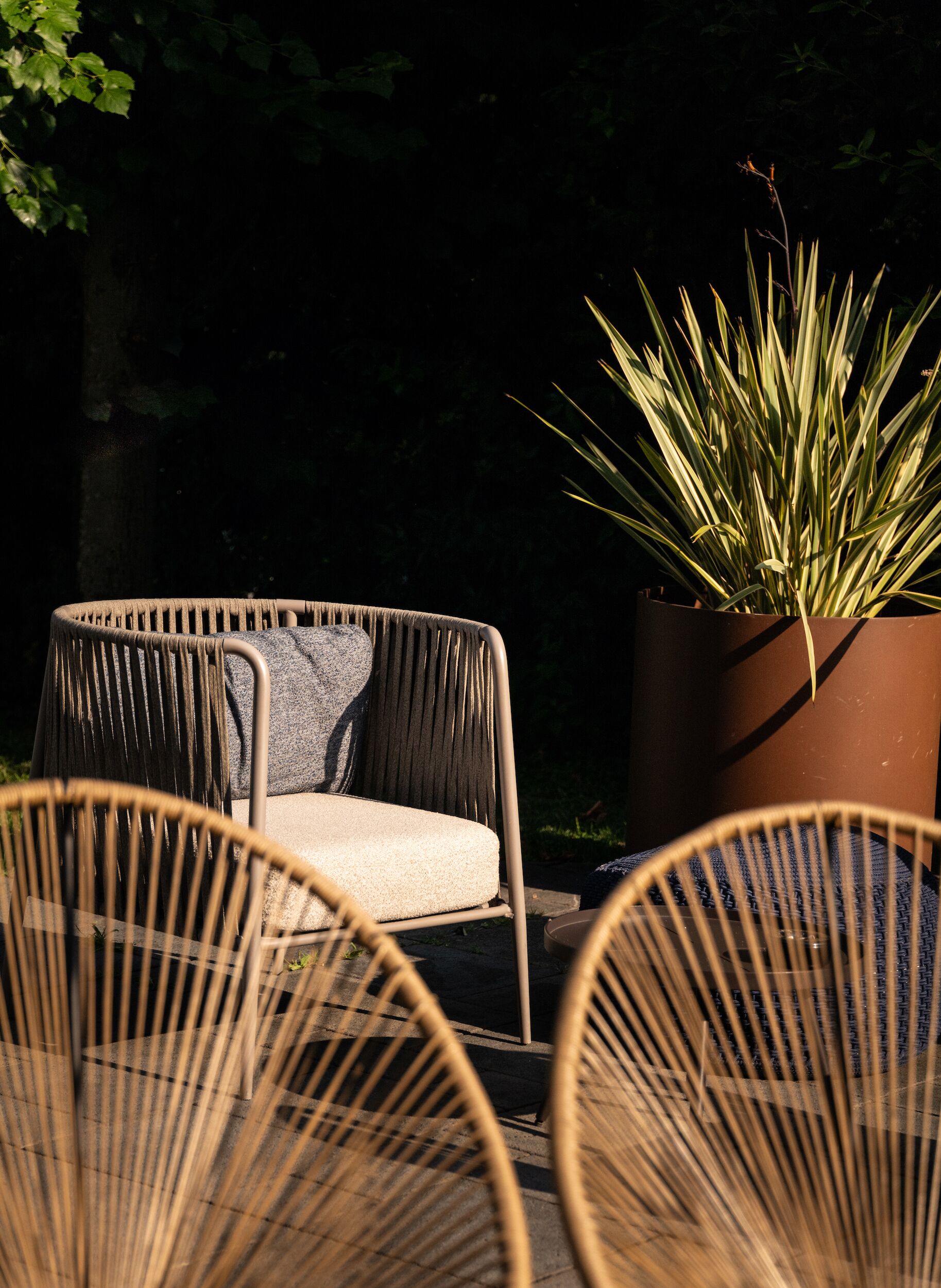 Des chaises en osier avec des coussins, une plante en pot et une table en bois, le tout installé dans un espace extérieur.