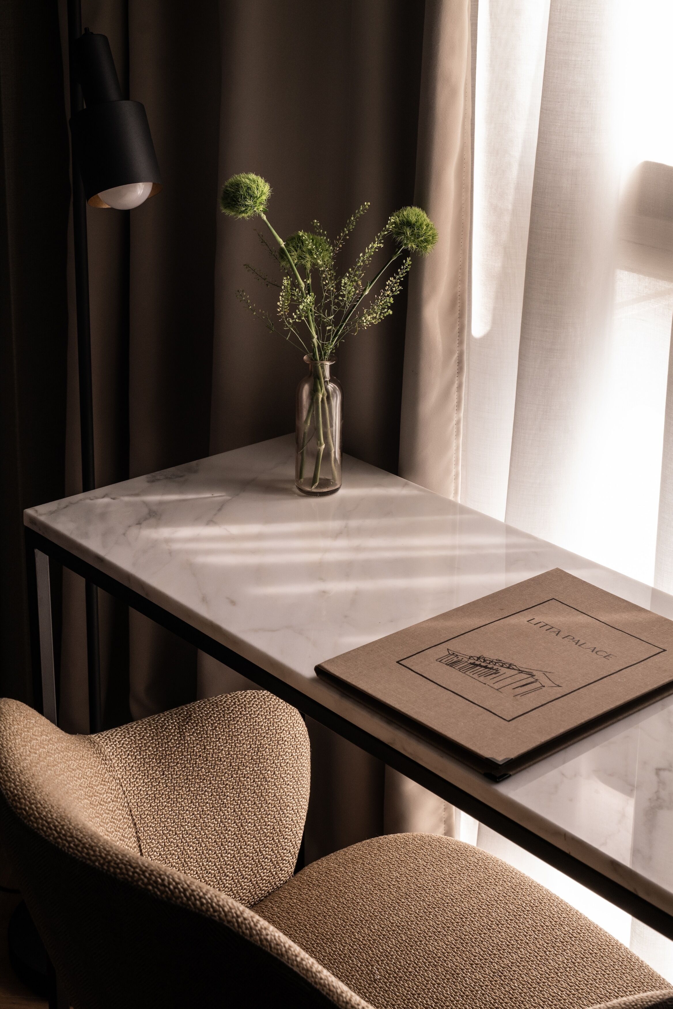 A modern room with a marble table, a vase with green plants, a framed picture, and a black lamp.