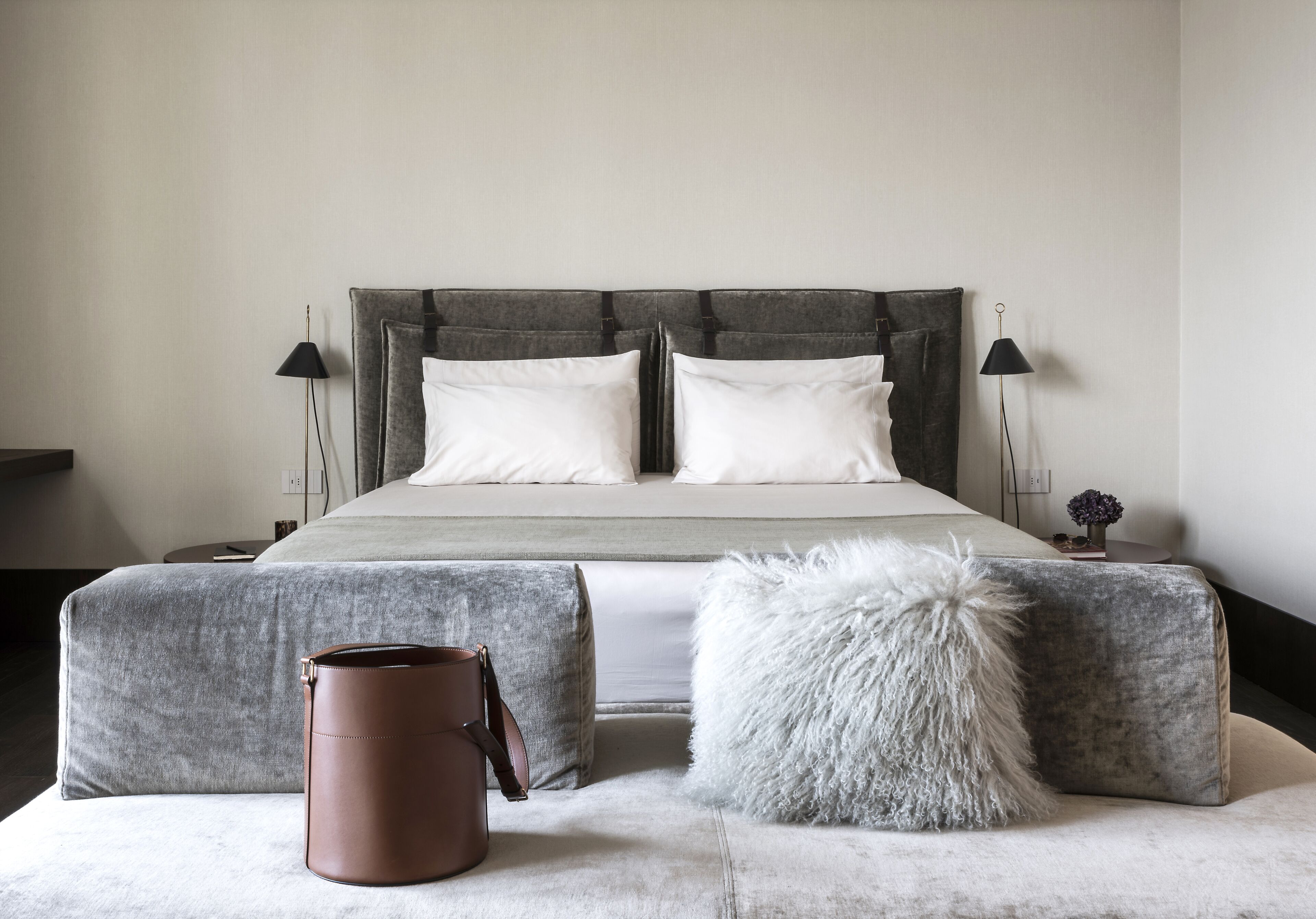 A modern bedroom with a large bed, two bedside lamps, a grey headboard, and a fluffy white pillow.