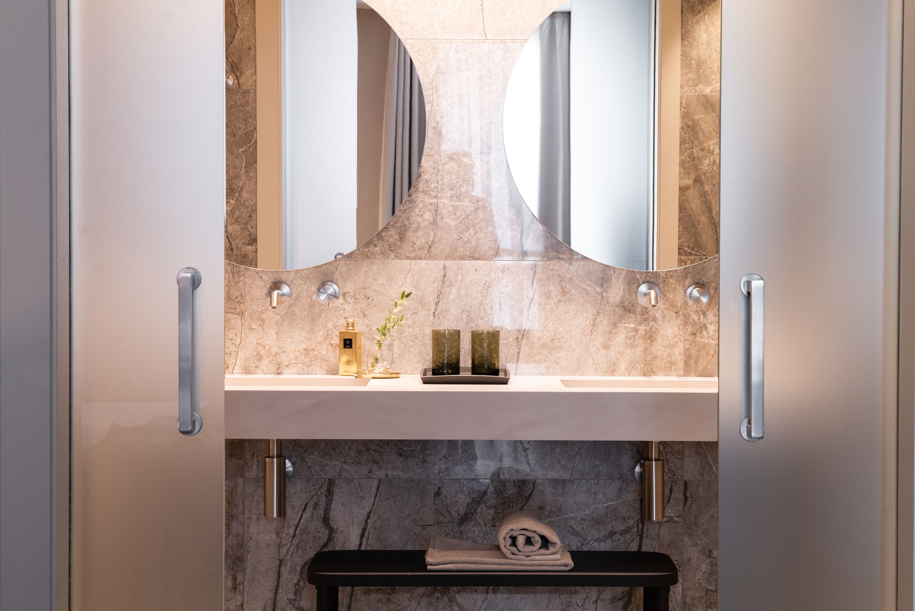 A bathroom with a marble vanity, a large mirror, and a towel bench.