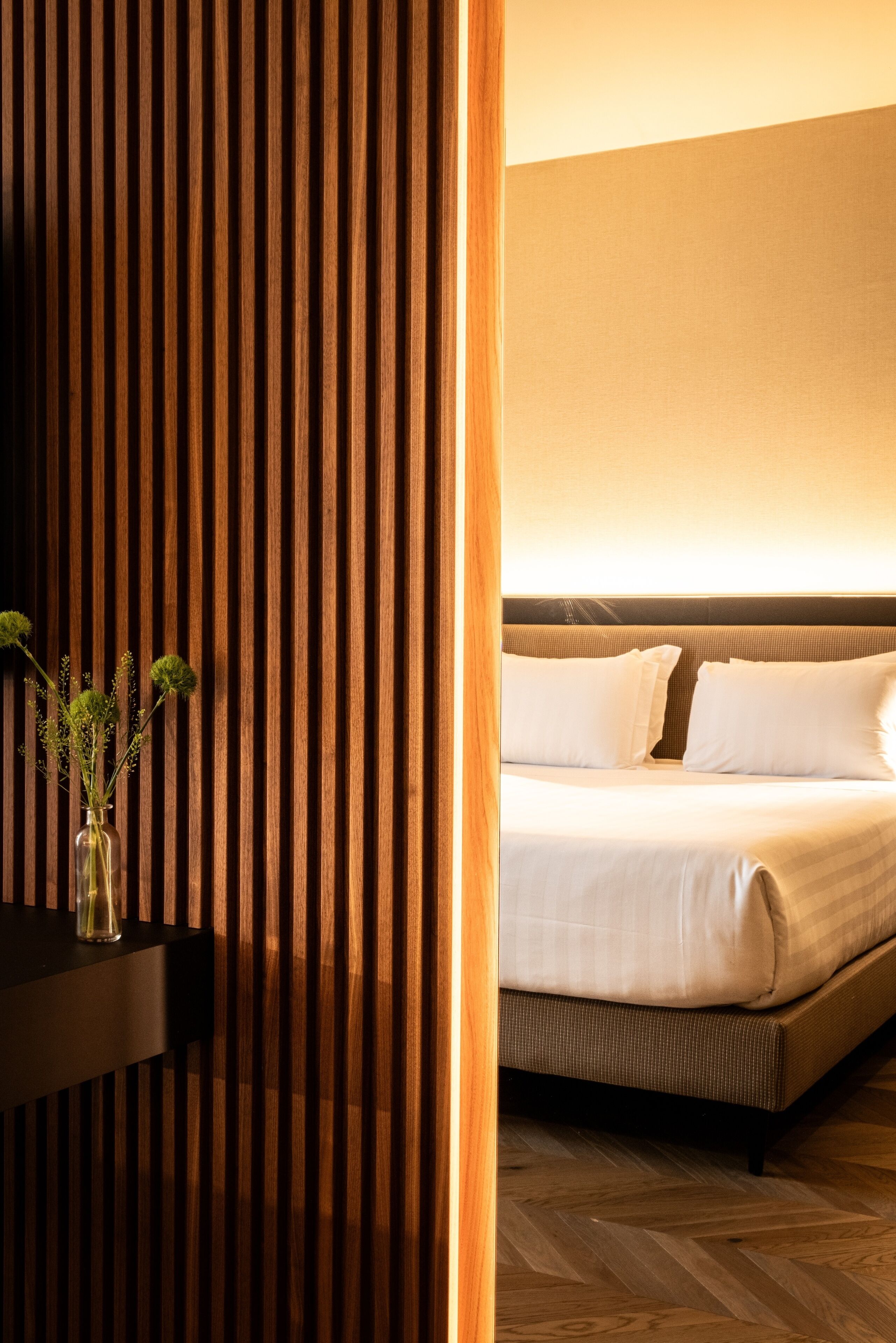 A hotel room with a bed, a nightstand, and a vase with flowers.