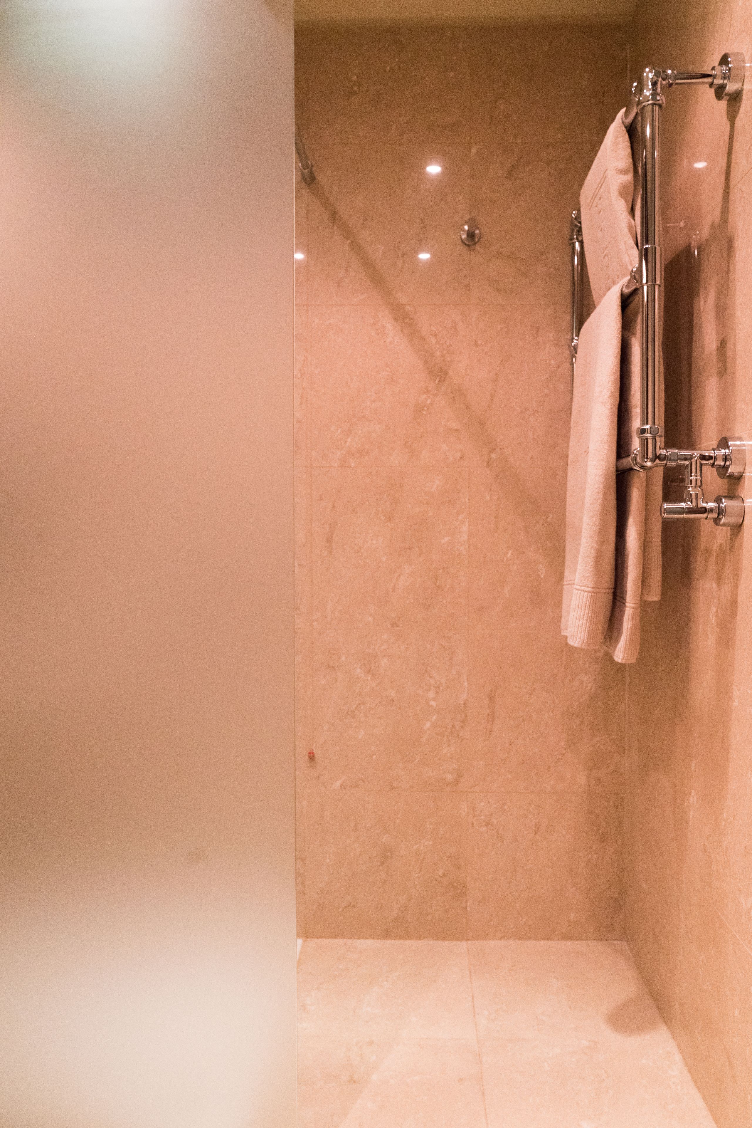 Baño con ducha, paredes de azulejos y un perchero con toallas.