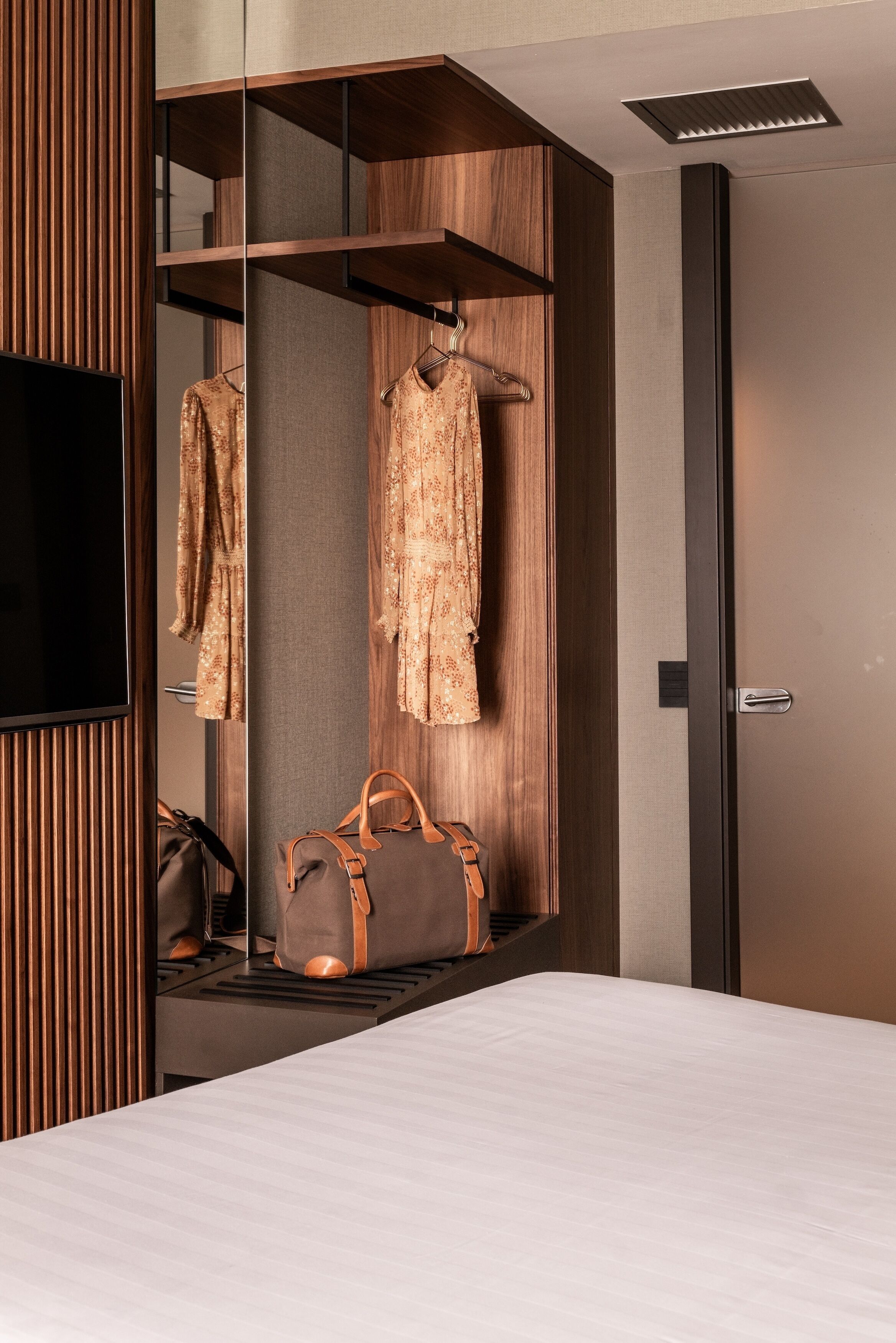 A hotel room with a bed, a wardrobe with hanging clothes, and a suitcase on the floor.