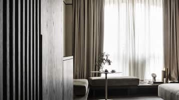 Una habitación de hotel moderna con piso de madera, un sofá, una pequeña mesa con una planta y una cama.