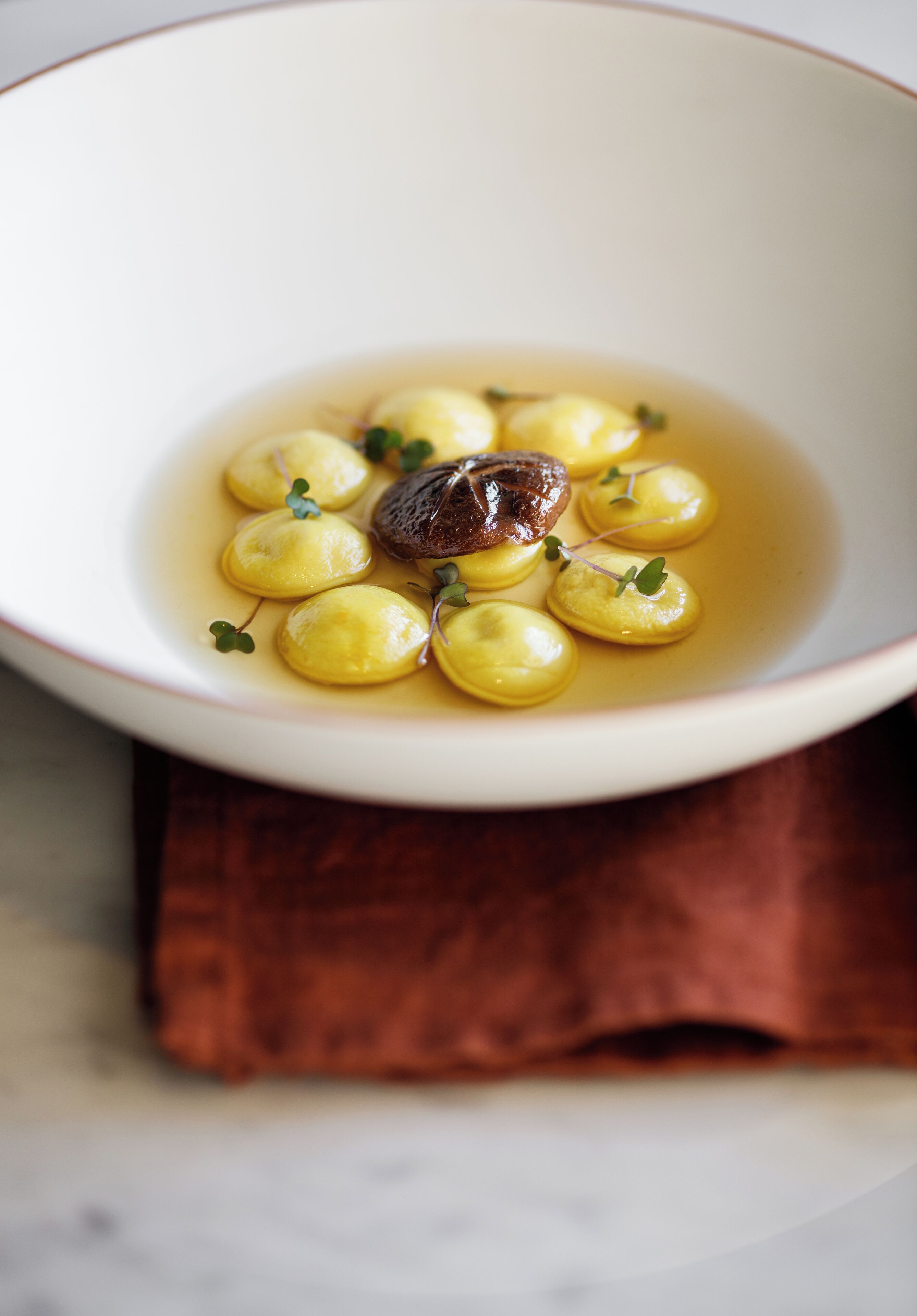 A white bowl with yellow dumplings and a piece of meat, placed on a brown napkin.