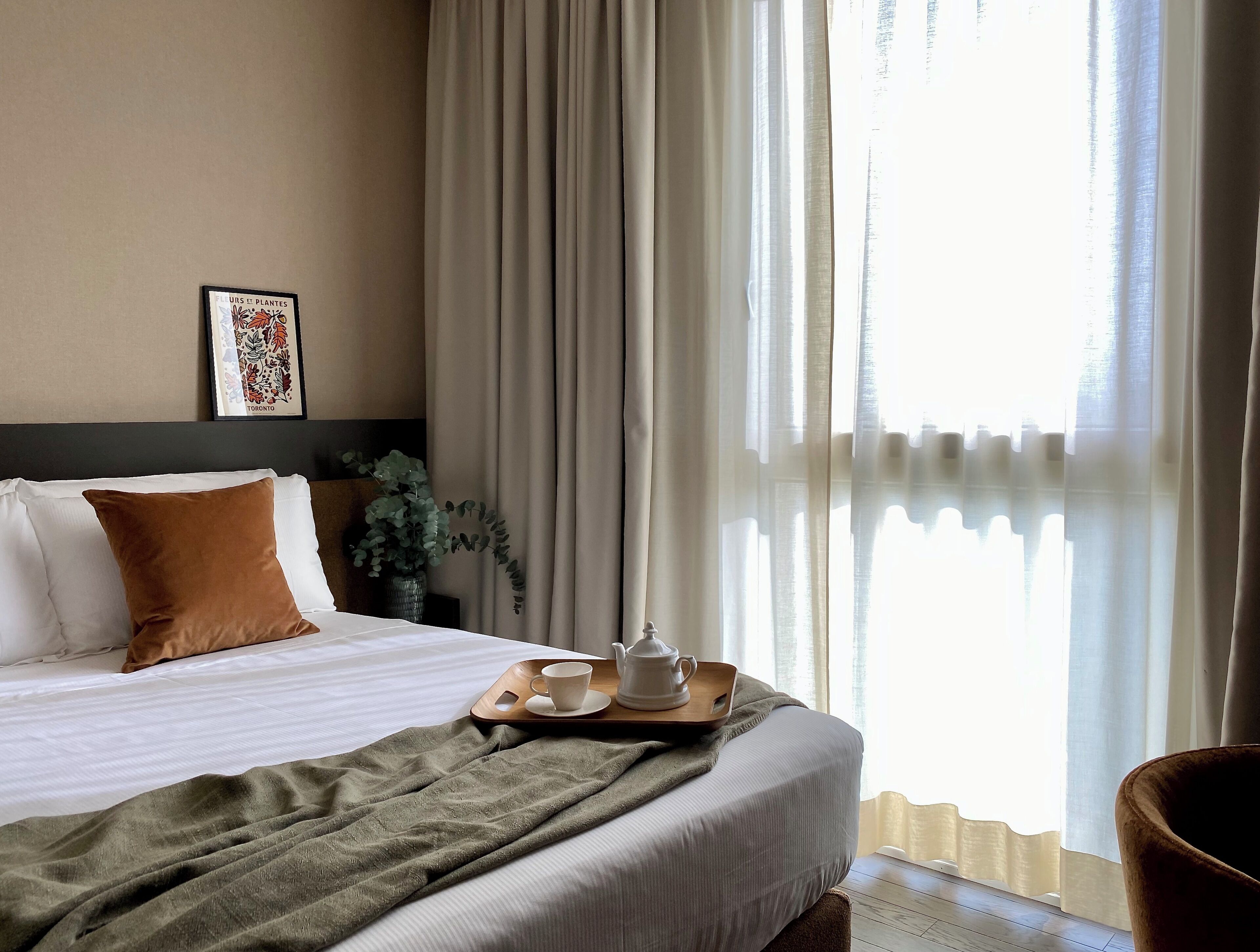 Habitación de hotel con cama bien hecha, una bandeja con tetera y taza, y un cuadro en la pared.