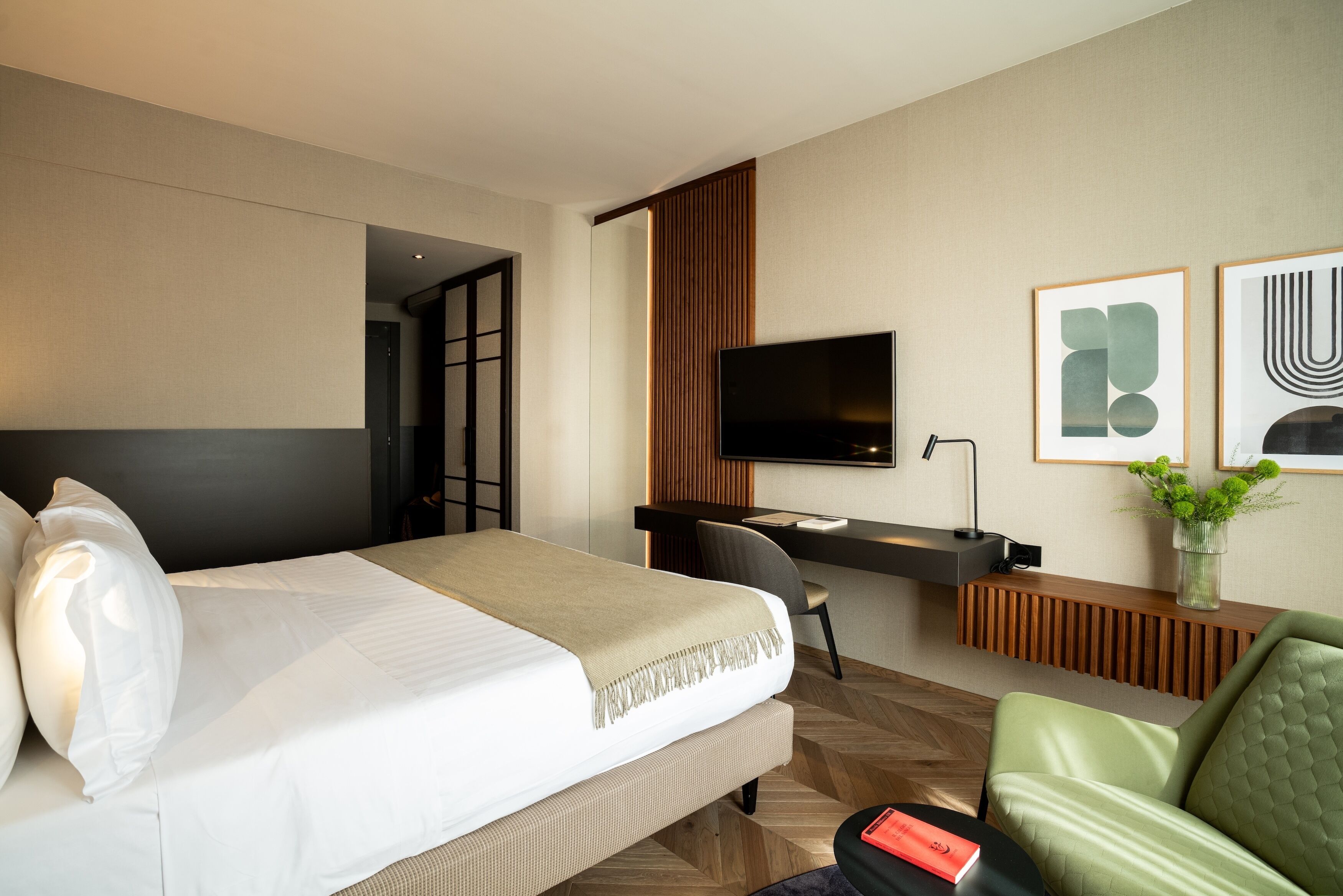 A hotel room with a bed, a desk, a TV, and a green sofa.