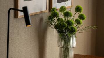 Ein gerahmtes abstraktes Kunstwerk an der Wand, eine moderne Schreibtischlampe und eine Vase mit kugelförmigen grünen Blumen.