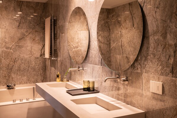 Un baño moderno con una bañera grande, dos lavamanos y espejos ovalados.