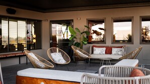 A modern outdoor seating area with wicker chairs and a sofa, large windows, and a potted plant. - Litta Palace Milano Urban Resort (Lainate)