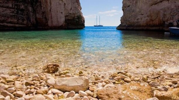 A rocky beach with clear water and a sailboat in the distance. - Vis Apartments (Vis)