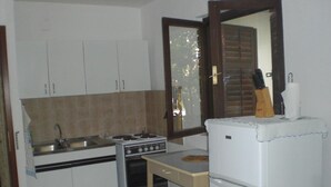 A compact kitchen with white cabinets, a stove, a sink, and a refrigerator. - Vis Apartments (Vis)