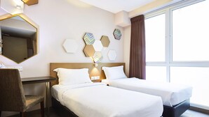 Een hotelkamer met twee bedden, een bureau, een stoel, een grote spiegel en decoratieve muurkunst.