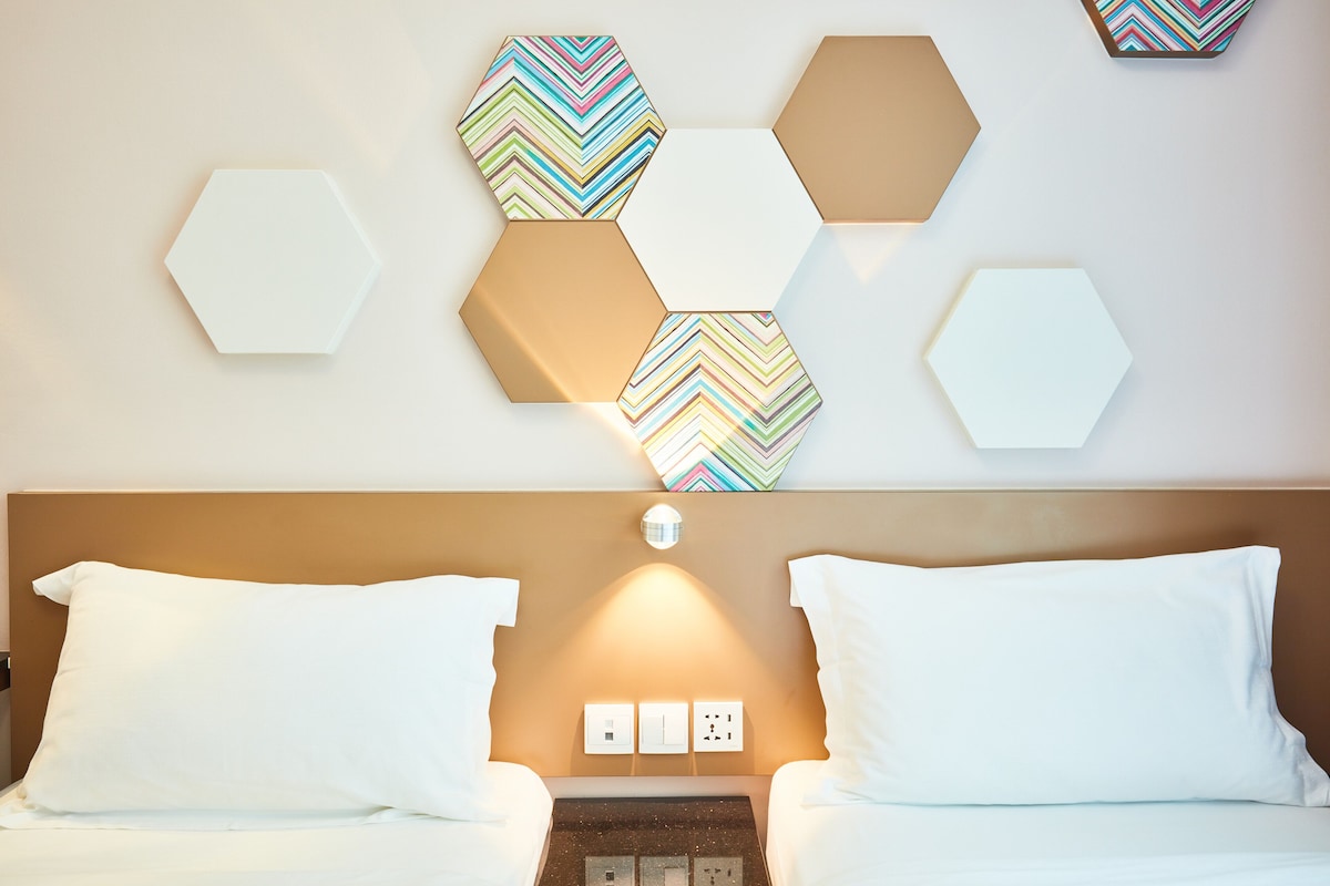 Una habitación de hotel con una cama, almohadas blancas, un cabecero y una pared decorada con piezas hexagonales.