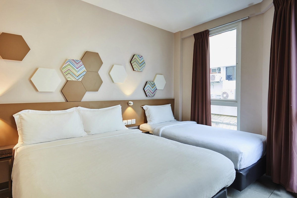 A hotel room with two beds, a large window with curtains, and hexagonal wall decor.