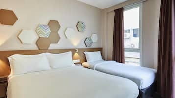 A hotel room with two beds, a large window with curtains, and hexagonal wall decor.